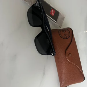 Svarta Wayfarer solglasögon från Ray-Ban - Klassiska svarta Wayfarer solglasögon från Ray-Ban med mörka glas och tydlig logga på skalmen. Säljs med original brunt fodral och putsduk. Perfekt accessoar för soliga dagar.