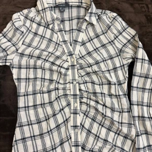 Vit och svart rutig skjorta från Primark - Säljer en klassisk vit och svart rutig skjorta från Primark som är helt nytt aldrig använt. Skjortan har långa ärmar, knappar framtill och är tillverkad i ett mjukt bomullsmaterial. Perfekt för en avslappnad och stilren look.