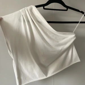 Vit one shoulder topp - Säljer en stilren vit one shoulder topp med draperad effekt över axeln. Super fin och passar till alla tillfällen 