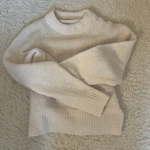 Krämvit stickad tröja med rund hals - Mysig beige stickad tröja med rund halsringning och långa ärmar. Tröjan ribbade muddar vid ärmslut och aldrig använd. Kontakta mig vid frågor 💕