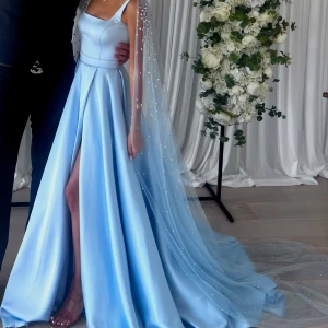 Ljusblå långklänning med slits och avtagbart pärl släp från axlarna - Egen designad och uppsydd ljusblå galaklänning och avtagbart släp på axlarna med ljusblåa pärlor, endast använd en kväll. Nypris 10 000kr