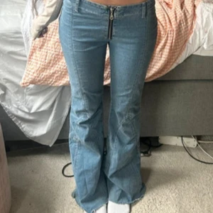 Ljusblå bootcut jeans med dragkedja - Säljer ett par ljusblå jeans med bootcut-modell och markerad dragkedja framtill. Jeansen har låg midja och är tillverkade i klassiskt denimtyg. Snygg passform som sitter tajt upptill och släpper vid benen.
