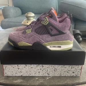 Nike Air Jordan 4 Retro lila mocka - Nike Air Jordan 4 Retro med lila mocka, gröna detaljer och svart mesh. Snygg kontrast med orange Jumpman-logga på plösen och svart hälpanel. Sulan är grönspräcklig och har synlig Air-enhet. Perfekta sneakers för dig som vill sticka ut. Skon är i mycket bra skick och använd fåtal gånger. Storlek 38,5 men passar upp till 39,5! Nypris gick för 3000 kr, säljer för 750, har tyvärr inte kvitto men va vänlig och gör din undersökning om du vill. Skulle du ha några frågor, ställ, pris kan diskuteras!