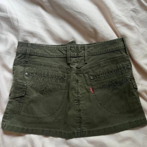 Grön jeanskjol från Levi's - Snygg olivgrön kortkjol från Levi's med broderade detaljer på bakfickorna, flera fickor och coola knappar. Knappt använd💕