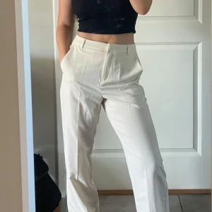 Beiga raka kostymbyxor - Stilrena beiga/vita kostymbyxor med raka ben och klassisk passform. Byxorna har hällor för bälte och dold dragkedja framtill. Perfekta för en clean och enkel look. Materialet känns mjukt och lätt, vilket gör dem sköna att bära hela dagen.