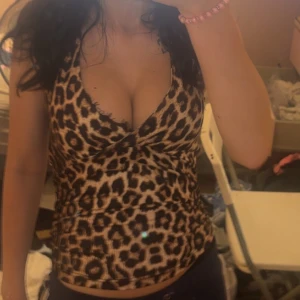 Leopardmönstrad omlottopp med knyt - Säljer en snygg leopardmönstrad omlottopp med djup v-ringning och knyt i nacken. Toppen är ärmlös och har en figurnära passform som framhäver siluetten. Perfekt för dig som vill sticka ut med ett djuriskt mönster och cool stil.