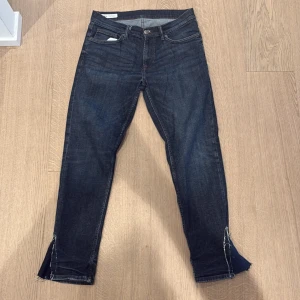 Zara Jeans med custom flare  - Säljer ett par mörkblå jeans med råa, slitna kanter och slits nertill vid bensluten. Jeansen har klassisk femficksdesign och smal passform. Perfekta för dig som gillar en edgy och avslappnad stil.