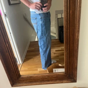 Blå jeans från Nudie med raka ben - Säljer ett par klassiska blå jeans från Nudie med raka ben och normal passform. Jeansen har snygga detaljer på bakfickorna och är tillverkade i bomull. Perfekta för dig som gillar en avslappnad och tidlös stil. Förhandlingsbart pris 