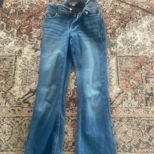 Blå lågmidjade bootcut jeans från Gina Tricot - Snygga blå jeans från Gina Tricot med bootcut-modell och klassisk femficksdesign. Jeansen har normal passform och är tillverkade i ett mjukt denimtyg som sitter skönt hela dagen. Perfekta för dig som gillar en retroinspirerad look. Brodyr på baksida fickor. Superfint skick.
