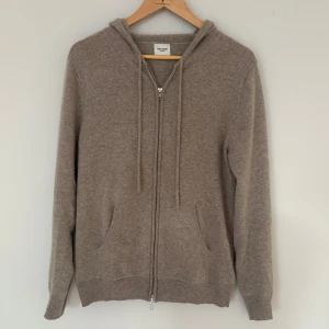 Beige kashmirhoodie från John Henric - Mjuk och lyxig hoodie i beige kashmir från John Henric. Tröjan har dragkedja framtill, huva med snörning och två fickor. Perfekt för dig som gillar en clean och avslappnad stil med premiumkänsla.