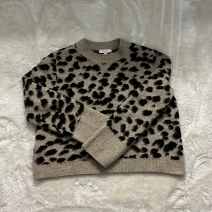 Beige leopardmönstrad stickad tröja H&M - Säljer en beige stickad tröja från H&M i storlek M med svart och mörkbrunt leopardmönster. Tröjan har rund hals, ribbade muddar och lång ärm. Perfekt för dig som vill sticka ut med ett djurmönster i höst och vinter.