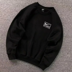 Svart sweatshirt från Nike  - Svart sweatshirt med rund hals och vit Nike x Stussy-logga på bröstet. Tröjan har långa ärmar, ribbade muddar och en klassisk, avslappnad passform. Perfekt för en streetwear-look och enkel att matcha med jeans eller joggers.
