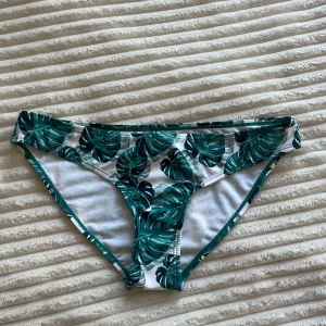 Gröna bikiniunderdel Andy by Frank Dandy - Snygg bikiniunderdel från Andy by Frank Dandy med tropiskt bladprint i grönt på vit botten. Klassisk brief-modell med låg midja och elastiska kanter. Perfekt för strandhäng och poolparty. De är ganska låga i midjan 😱 