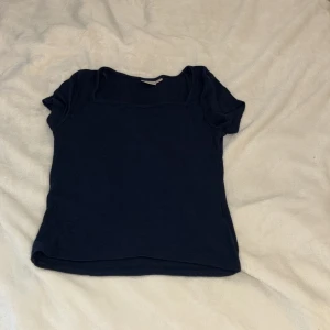 Mörkblå topp från Gina Tricot - En enkel och stilren mörkblå topp från Gina Tricot. Modellen har korta ärmar och en rundad halsringning. Perfekt att matcha med jeans eller kjol för en clean look. Mjuk och skön i materialet, passar dig som gillar basic men snyggt.