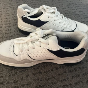 Vita sneakers - Snygga vita sneakers från 157 i storlek 39. Skorna har svarta detaljer på sidan och grå mockaliknande partier vid tån. Jag har bara använt dem två gånger och säljer på grund av att dem inte kommer till användning. 