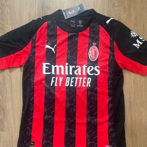 AC Milan 25/26 Fotbollströja - AC Milan matchtröja från Puma med klassiska röda och svarta ränder, klubbmärke på bröstet och sponsortryck framtill. Tillverkad i lätt och ventilerande polyester med DryCell-teknologi. Kortärmad modell med rund hals och snygga detaljer på axlarna.                                                  Nya säsongens fotbollströja (2025/2026) i storlek S.