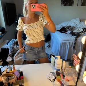 Vit croppad prickig blus med puffärm - Superfin vit croppad blus med svarta prickar och puffiga korta ärmar. Smockad överdel som sitter tajt och volangkant nertill. Offshoulder-modell som ger en söt och trendig vibe, perfekt till jeans eller kjol.