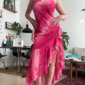 Rosa blommig långklänning med volang - Supersnygg långklänning i olika rosa nyanser med blommigt mönster och glittriga detaljer. Klänningen har smala axelband, asymmetrisk volangkant och omlottkänsla. 