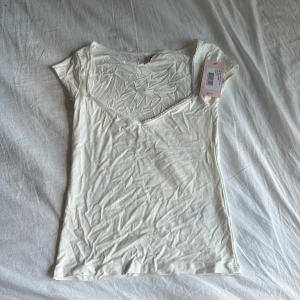 Vit v-ringad topp från Nelly XS - Säljer en söt vit topp från Nelly i storlek XS. Toppen har v-ringning med spetskant,  är kortärmad och är helt ny!