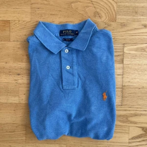 Ralph Lauren piké  - Klassisk blå pikétröja från Polo Ralph Lauren i slim fit-modell. Tillverkad i mjuk bomull som känns skön mot huden. Storlek M.
