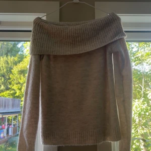 Beige offshoulder stickad tröja Gina Tricot - Supermysig beige stickad tröja från Gina Tricot med bred ribbad offshoulder-krage. Perfekt för dig som gillar en chill och snygg stil. Långärmad och i mjukt material som håller dig varm under kyliga dagar.