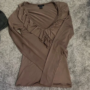 Brun långärmad topp med volang - Säljer en brun långärmad topp från New yorker i stretchigt material. Toppen har v-ringning och en snygg volangdetalj framtill.