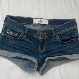 Hollister jeansshorts - Snygga mörkblå jeansshorts från Hollister med klassisk femficksdesign, uppvikta benslut och kontrastsömmar. Shortsen har låg midja och coola detaljer på bakfickorna. Säljer för dem it kommer till användning 