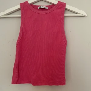 Rosa ribbad linnetopp från Zara - Säljer en snygg rosa ribbad linnetopp från Zara. Toppen är ärmlös med rund halsringning och croppad passform. Perfekt för varma dagar och enkel att matcha med jeans eller kjol. Storlek S. 