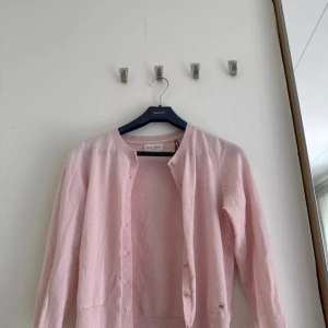 Ljusrosa kofta från Holly & Whyte - Supersöt ljusrosa kofta från Holly & Whyte by Lindex. Koftan har rund hals, långa ärmar och snygga guldfärgade knappar framtill. perfekt att slänga över en topp när det är lite kyligt ute.