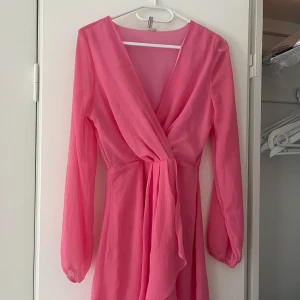 Rosa omlottklänning med lång ärm - Supersöt rosa kortklänning. Långa ärmar i lätt, luftig polyester ger en flowy känsla.