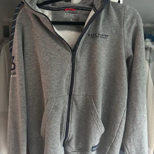 Grå hoodie från Race Marine med dragkedja - Säljer en grå hoodie från Race Marine i storlek S. Tröjan har hel dragkedja, huva med snörning och broderad logga samt siffran 83 på ärmen. Mjuk insida och två fickor framtill. Perfekt för chill dagar eller när du vill ha en sportig look.