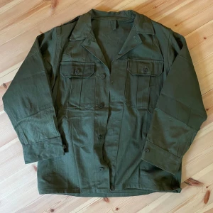 Grön overshirt med fickor - Snygg militärgrön overshirt med klassisk krage och två stora bröstfickor med knappar. Jackan har raka ärmar och stängs med knappar framtill. Perfekt för lager-på-lager och chill stil.