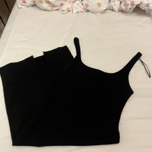 Svart linnetopp från Zara Trafaluc - En stilren svart linnetopp från Zara Trafaluc med smala axelband och rak, croppad passform. Perfekt att matcha med höga jeans eller kjol. Tidlös design som funkar till många olika looks.