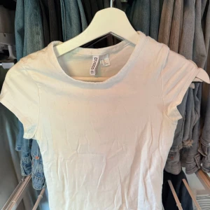 Vit basic t-shirt från H&M Divided XS - Enkel och fräsch vit t-shirt från H&M Divided i storlek XS. Modellen är klassisk med rund halsringning och korta ärmar. Perfekt att matcha med jeans eller kjol för en clean och stilren look. Tröjan slutar runt midjan och sitter tajt.