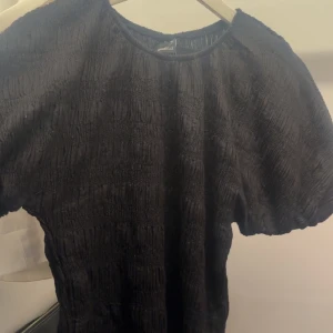 Svart ribbad topp från Gina Tricot - HELT NY.Säljer en svart ribbad topp från Gina Tricot i storlek M. Toppen har korta ”puff” ärmar och en smockad struktur som ger en cool och trendig look. Perfekt att styla med jeans eller kjol för en snygg outfit.  Passar mig som brukar bära strl S.