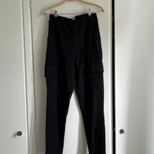 Svarta cargopants från Gina Tricot - Svarta cargopants från Gina Tricot i ribbad polyester. Byxorna har hög midja, resår i midjan och stora fickor på sidorna. Stretchiga o snygga.