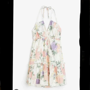 Blommig sommarklänning med volang - Supersöt kort blommig klänning med volangkant och knyt i nacken. Ljus bas med pastelliga blommor i rosa, lila och grönt. Djup v-ringning och ärmlös design, perfekt för varma dagar. Luftigt material som känns skönt mot huden. Från HM