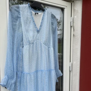 Ljusblå volangklänning Vero Moda M - Supersöt ljusblå kortklänning från Vero Moda med vittmönster, v-ringning och volangdetaljer vid ärmslut,krage och nederkanten på klänningen. Klänningen har långa, transparenta ärmar och är fodrad. Perfekt för sommarens alla tillfällen!