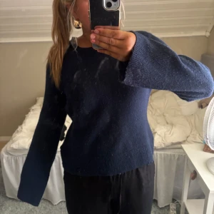 Mörkblå stickad tröja med vida ärmar - Mysig mörkblå stickad tröja med rund halsringning och långa, lite vidare ärmar. Enkel och stilren modell som passar perfekt till jeans eller mjukisbyxor. Skön att bära under kyligare dagar och lätt att matcha med olika outfits.