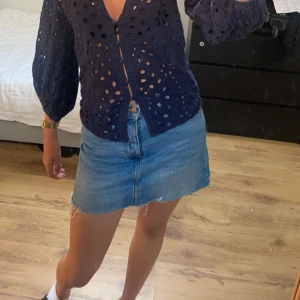Blå jeanskjol  - Säljer en klassisk blå jeanskjol i kort modell med rå, fransig nederkant. Kjolen har en enkel design med synliga sömmar och knapp framtill. Perfekt för dig som gillar en avslappnad och trendig stil.