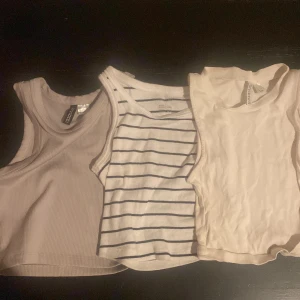3-pack croppade linnetoppar - Säljer tre croppade linnetoppar i olika stilar. En beige ribbad från Gina Tricot, en vit med svarta ränder från Cubus och en enkel vit. Alla är ärmlösa och perfekta för varma dagar eller lager på lager. Snygga att matcha med jeans eller kjol.