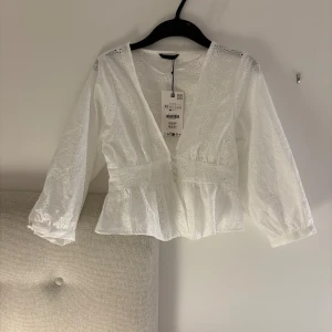 Vit broderad blus från Zara XS - Superfin vit blus från Zara i storlek XS med broderade blommor och v-ringning. Blusen har långa ärmar, knappar framtill och lätt volang nedtill. Perfekt för en fräsch och romantisk look.