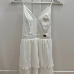 Vit kortklänning  - Superfin vit kortklänning från Chiara Forthi med smala axelband, v-ringning och plisserad kjol. Klänningen har justerbara band i ryggen och en elegant, stilren look. 