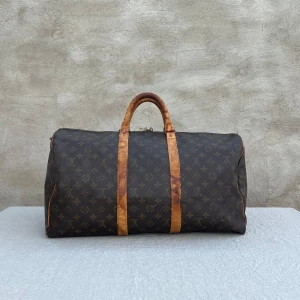 Louis Vuitton Keepall monogram resväska - Klassisk Louis Vuitton Keepall resväska i brunt monogrammönster med ikoniska LV-loggor. Väskan har detaljer och handtag i ljust skinn, guldfärgad dragkedja och rymlig form. Perfekt för weekendresor och har den där lyxiga vintagekänslan.