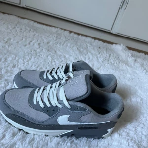Nike Air Max 90 greay smoke limited edition  - Snygga Nike Air Max 90 sneakers i olika grå nyanser med vita detaljer och klassisk vit swoosh. Ovandel i textil och syntet, med vit snörning och robust sula. Perfekta för dig som gillar stilrena och sportiga skor med ikonisk design.