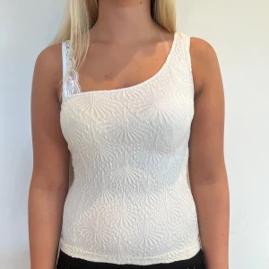 Vit asymmetrisk topp med spetsdetalj - Säljer en vit, figurnära topp som är one shoulder.