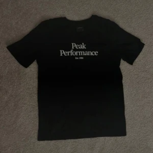 Svart Peak Performance t-shirt - Svart t-shirt från Peak Performance med vit logga och texten 'Est. 1986' på bröstet. Klassisk rund hals och korta ärmar. Oanvänd. 