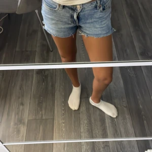 Blå jeansshorts med fransig kant - Säljer ett par klassiska blå jeansshorts med fransig kant och femficksmodell. Shortsen har låg midja och en avslappnad passform. Perfekta för varma sommardagar och ger en cool, avslappnad vibe.