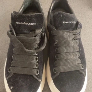 Svarta sneakers från Alexander McQueen - Stilrena svarta sneakers från Alexander McQueen med breda svarta snören och vit sula. Ovandelen är i mocka och har logga på plösen. Perfekta för dig som gillar en clean och lyxig look. nypris är runt 6k men eftersom jag ej behöver dessa så kan jag diskutera priset!! dustbag, låda, serienummer finns!!