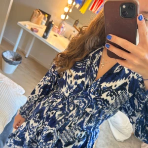 Blåvit kortklänning från Zara - Supersnygg blåvit kortklänning från Zara med coolt abstrakt mönster. Klänningen har v-ringning, långa ärmar med resår vid handlederna och markerad midja. 